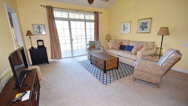 A living room with a sofa, armchair, coffee table, and a television on a wooden stand. - Cypress Bend Apartment 532 (North Myrtle Beach)