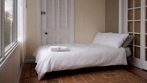 A single bed with white bedding in a room with a door and a window.