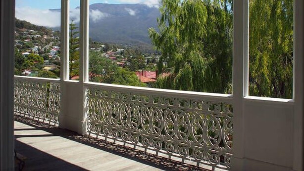 A balcony with ornate white railings and a view of a town and mountains in the distance.