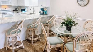 A kitchen with white cabinets, a microwave, a coffee station, and a glass dining table with wicker chairs. - *Fall into Savings-20% Off New Bookings thru 2026* (Surfside Beach)