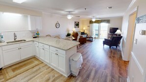 A spacious kitchen with white cabinets, a granite countertop, and a wooden floor. There is a dining area with a table and chairs, and a living room with a sofa and a television. - *Fall into Savings-20% Off New Bookings thru 2026* (Surfside Beach)