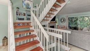 Una escalera con barandillas blancas y escalones de madera que conduce a una sala de estar con un sofá gris y una chimenea.