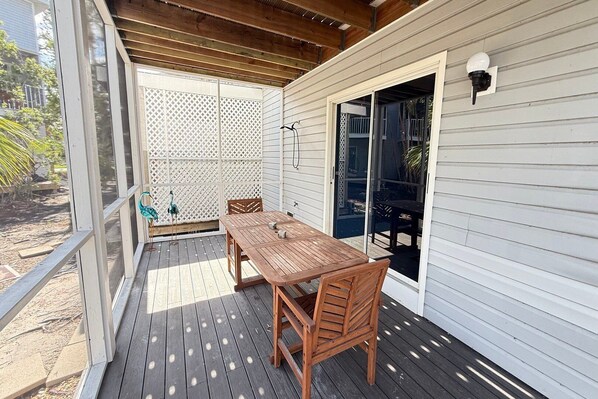 A covered patio with a wooden table and chairs, a sliding glass door, and a white fence.