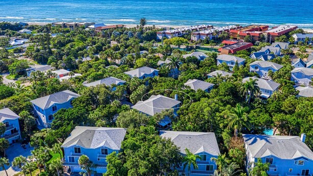 Vista aérea de una zona residencial costera con casas rodeadas de exuberante vegetación y una playa al fondo.