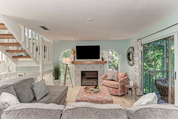 Ein geräumiges Wohnzimmer mit Kamin, großem Fernseher und einem Balkon mit Gartenmöbeln.