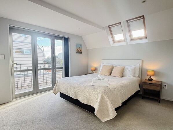 A bedroom with a bed, two bedside lamps, a sliding glass door, and a small painting on the wall.