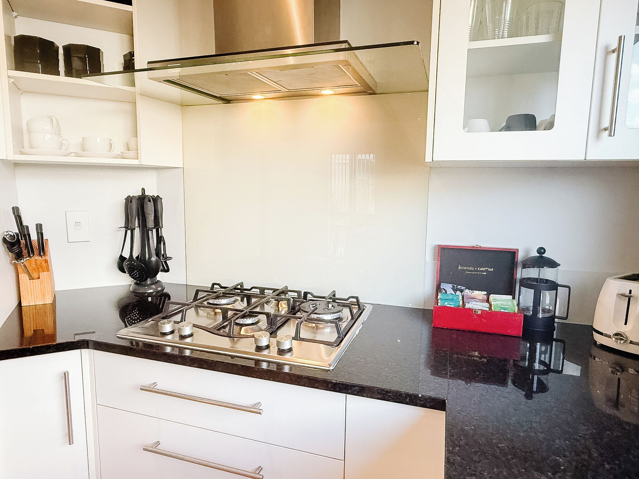 Une cuisine moderne avec des meubles blancs, une cuisinière à gaz, une machine à café et un grille-pain.