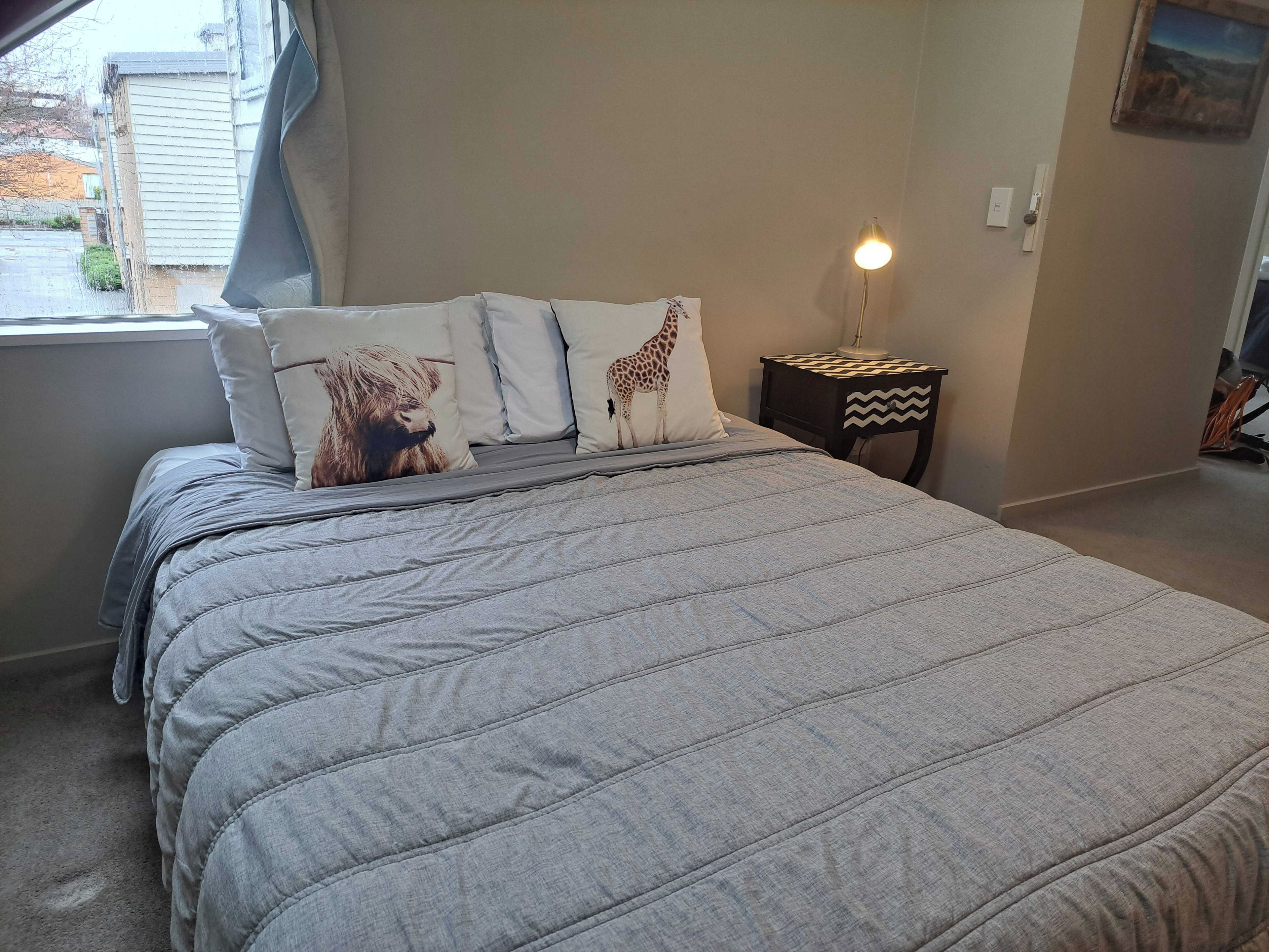 Ein Schlafzimmer mit Bett, Kissen, einem Nachttisch und einer Lampe.