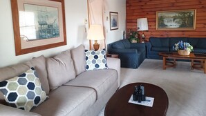 A living room with a beige sofa, a blue patterned sofa, a wooden coffee table, and a wooden wall with a painting. - Lakefront Log Home w/ Dock Slip, 30% Weekly Discount, 2 Miles from Nat. Park (Swanton)