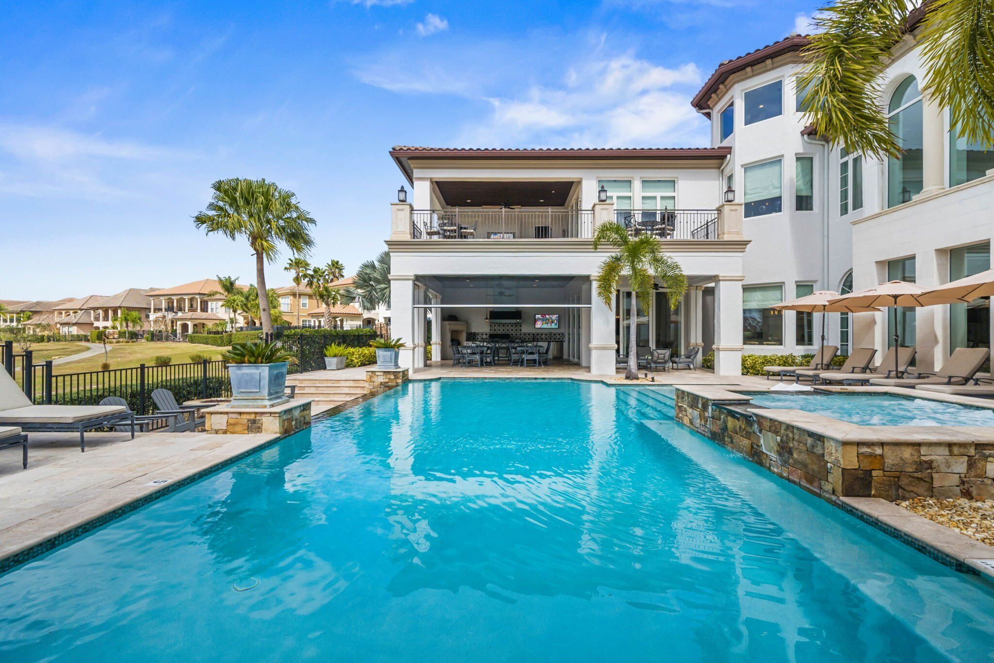 A swimming pool with lounge chairs and umbrellas, surrounded by a two-story building with balconies.