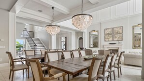 Une salle à manger spacieuse, dotée d’une grande table et de chaises en bois, de lustres élégants et d’un escalier menant à un niveau supérieur.