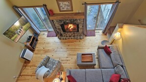 A cozy living room with a stone fireplace, a sofa, a television, and a fireplace screen. - 24 Rogue-Sunriver, Oregon: Hot Tub, BBQ, WiFi, SHARC Aquatics, Tubing Hill, Mt. Bachelor, Golf, Deschutes River, Tennis, Bike Paths (Sunriver)