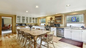 A spacious kitchen with white cabinetry, a wooden dining table, and a large window with a view of trees. - 24 Rogue-Sunriver, Oregon: Hot Tub, BBQ, WiFi, SHARC Aquatics, Tubing Hill, Mt. Bachelor, Golf, Deschutes River, Tennis, Bike Paths (Sunriver)
