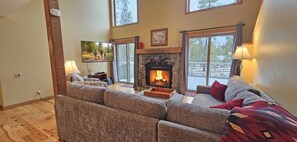 A cozy living room with a fireplace, comfortable seating, and large windows.