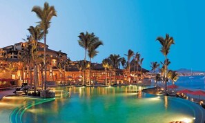 A resort with a large infinity pool, palm trees, and a view of the ocean at dusk. - HACIENDA BEACH CLUB   OCEAN VIEW.  DIRECTLY ON MEDANO BEACH.  GREAT LOCATION  (Cabo San Lucas)