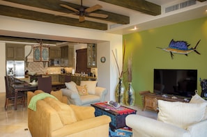 A spacious living room with a large flat-screen TV, comfortable seating, and a dining area with wooden cabinets and a chandelier.