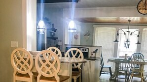 Un comedor con sillas de madera y una mesa, una cocina con estufa y refrigerador, y un reloj en la pared.