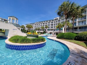 A hotel with a swimming pool, palm trees, and a multi-story building with balconies. - Bridgewater 301 - End Unit, Lazy River, Pool (Pawleys Island)