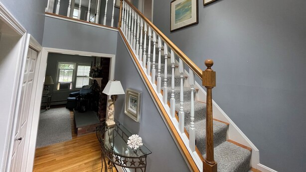 A staircase with a wooden handrail and white balusters, leading to a landing with a glass table and a white lamp. - Fun & Sun in Osterville MA - Sleeps 10, Beach Pass (Barnstable)