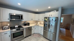 A modern kitchen with white cabinets, stainless steel appliances, and a tiled backsplash. - Fun & Sun in Osterville MA - Sleeps 10, Beach Pass (Barnstable)