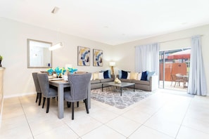 A modern living room with a dining area, a sofa set, and a large sliding glass door leading to an outdoor patio.