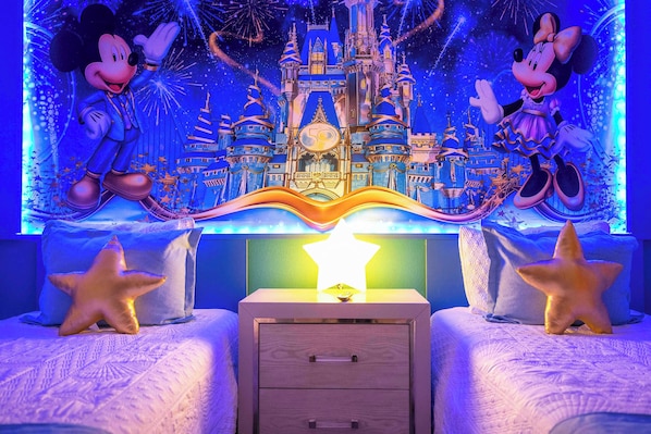 A bedroom with a Disney castle mural, two star-shaped pillows, and a nightstand with drawers.