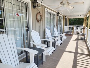 A covered porch with white Adirondack chairs and tables, a ceiling fan, and a decorative wreath.
