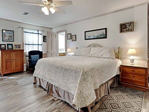 A bedroom with a large bed, a ceiling fan, a wooden wardrobe, a chair, and a patterned rug.