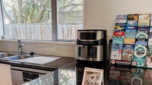 Una encimera de cocina con una cafetera, un lavamanos y una ventana con vistas a árboles.