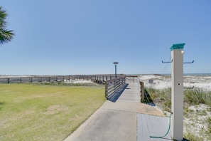 Stroll along the paved walkway to the serene beach, lined with a wooden railing and a lamp post.
