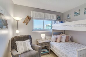 A cozy bedroom with a bunk bed, a chair, a bedside table with a lamp, and artwork on the walls. - Gulf Highlands Getaway w/ 6 Pools & Beach Access (Gulf Shores)