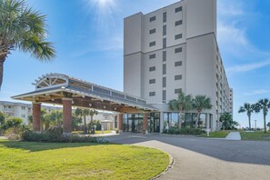 A modern hotel entrance with a covered walkway, palm trees, and a clear sky. - Gulf Highlands Getaway w/ 6 Pools & Beach Access (Gulf Shores)