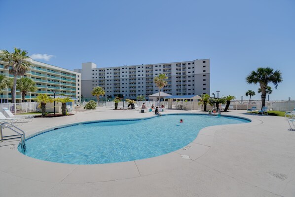 A swimming pool area with a pool, lounge chairs, and a hotel building in the background. - Gulf Highlands Getaway w/ 6 Pools & Beach Access (Gulf Shores)