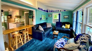 Una sala de estar acogedora con un sofá azul, una mesa de centro de madera y un comedor con una mesa y taburetes de madera.