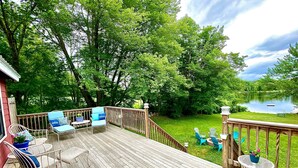 Una terraza de madera con mobiliario exterior, vista a un lago y un área con césped.