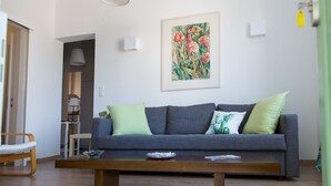 Ein modernes Wohnzimmer mit einem grauen Sofa, grünen Kissen, einem Holztisch und einem gerahmten floralen Gemälde an der Wand.
