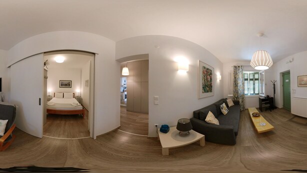 Ein modernes Wohnzimmer mit einer Couch, einem Couchtisch und einem Fernseher. Im angrenzenden Raum befindet sich ein Bett.