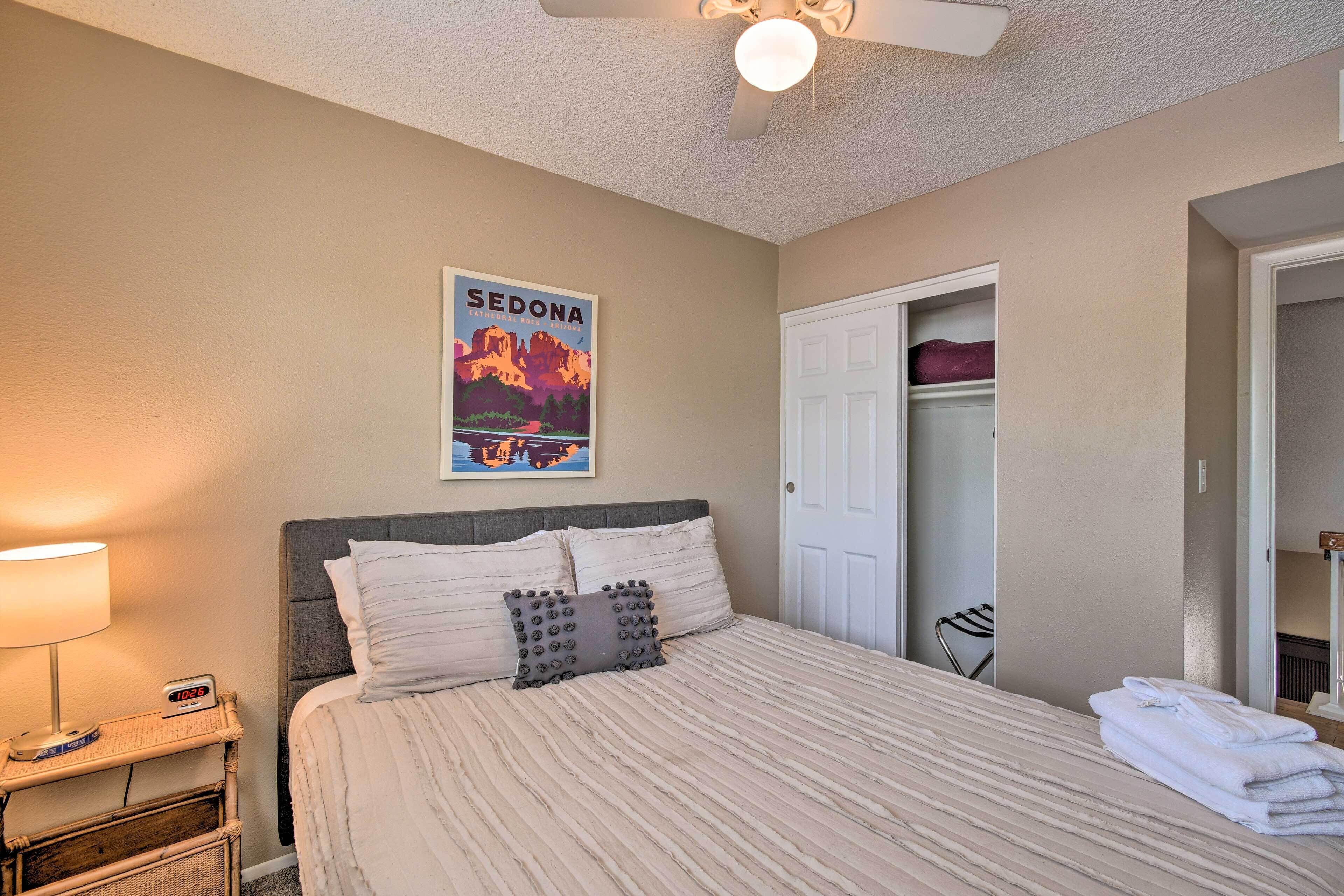 Un lit bien fait, avec une couvre-lit à rayures, un oreiller et une affiche de Sedona accrochée au mur.