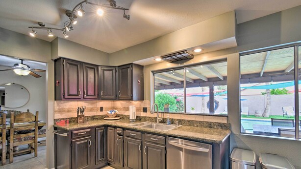 A modern kitchen with dark cabinets, stainless steel appliances, and a large window overlooking a patio area.