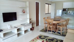 Sala de estar com televisão, móvel de entretenimento, mesa de jantar e cadeiras.