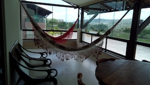 Uma rede em um quarto com janelas amplas, piso de azulejos e vista para a paisagem.