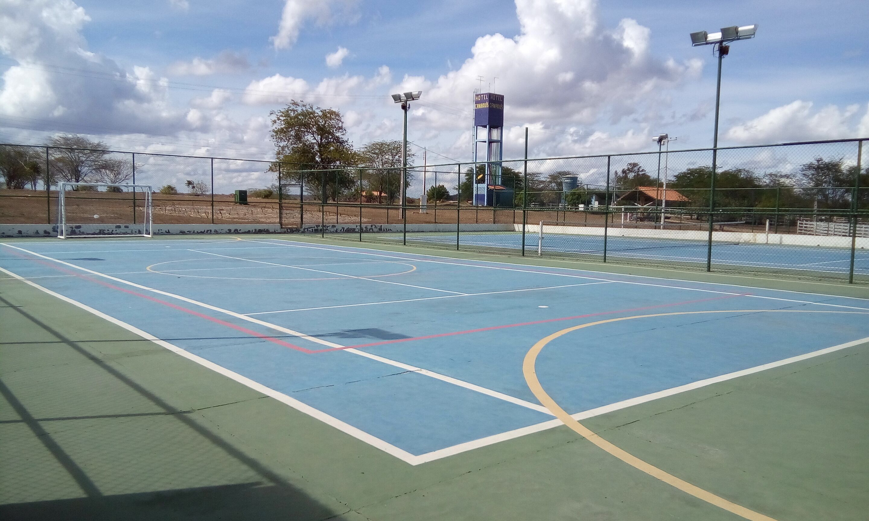 An outdoor basketball court with a fence, a sign for Hotel Conquist, and a clear sky.