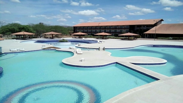 Uma grande piscina em vários níveis, com espreguiçadeiras e guarda-sóis, rodeada por um edifício com telhado vermelho.