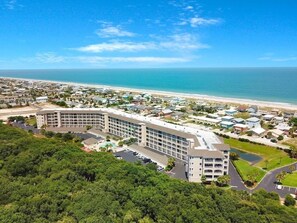 A large hotel with multiple floors, a parking lot, and a view of the beach and ocean.