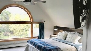 A bedroom with a large window, a bed, a ceiling fan, and a desk. - Updated Middlebury Home! Walk to Town, Sleeps Groups Comfortably (Middlebury)
