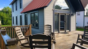 A house with a covered deck, a large window, and a sliding glass door. - Updated Middlebury Home! Walk to Town, Sleeps Groups Comfortably (Middlebury)