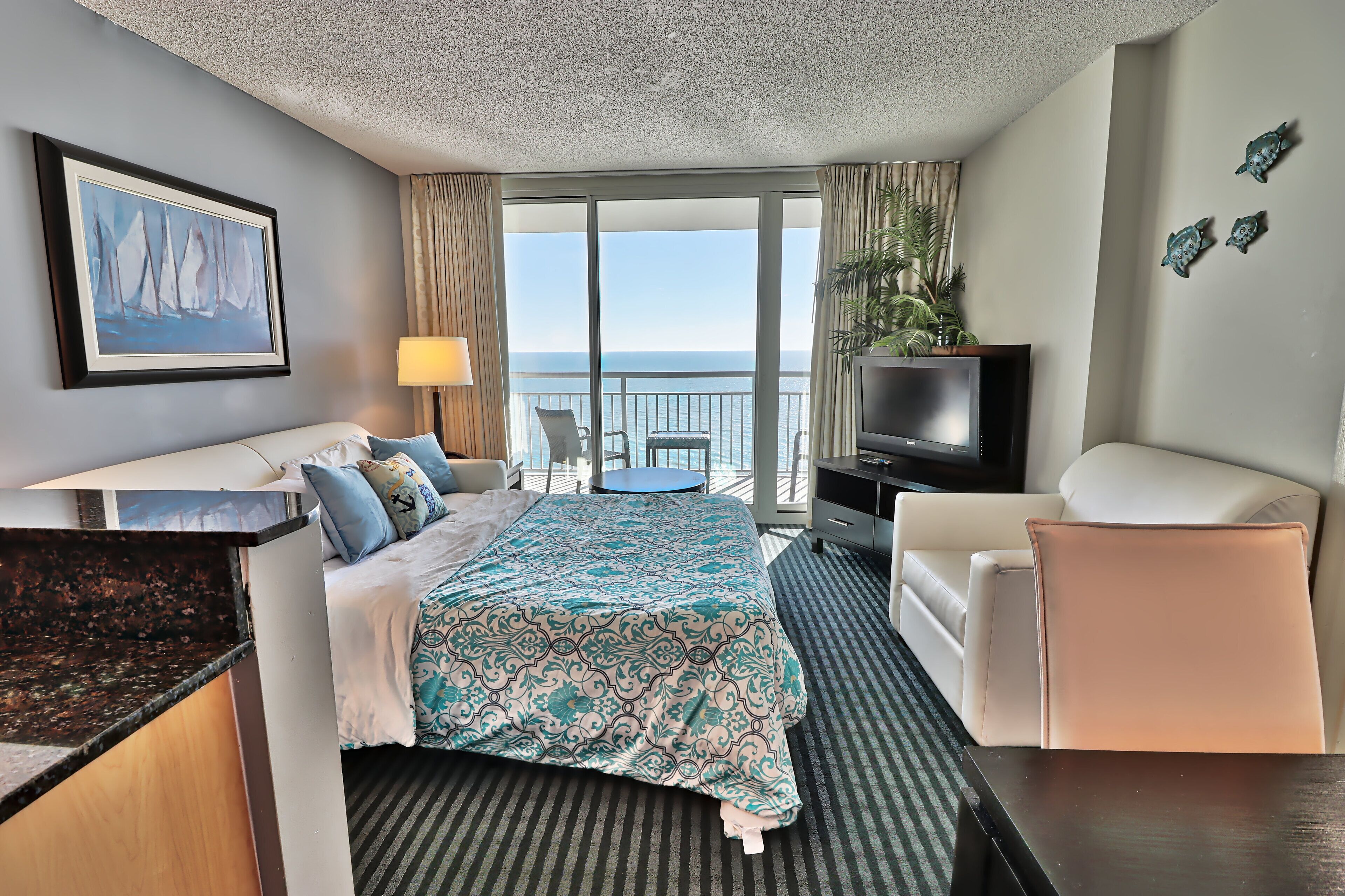 Une chambre d’h ôtel équipée d’un lit, d’une télévision, d’un bureau, d’une chaise et d’un balcon avec vue sur la mer.
