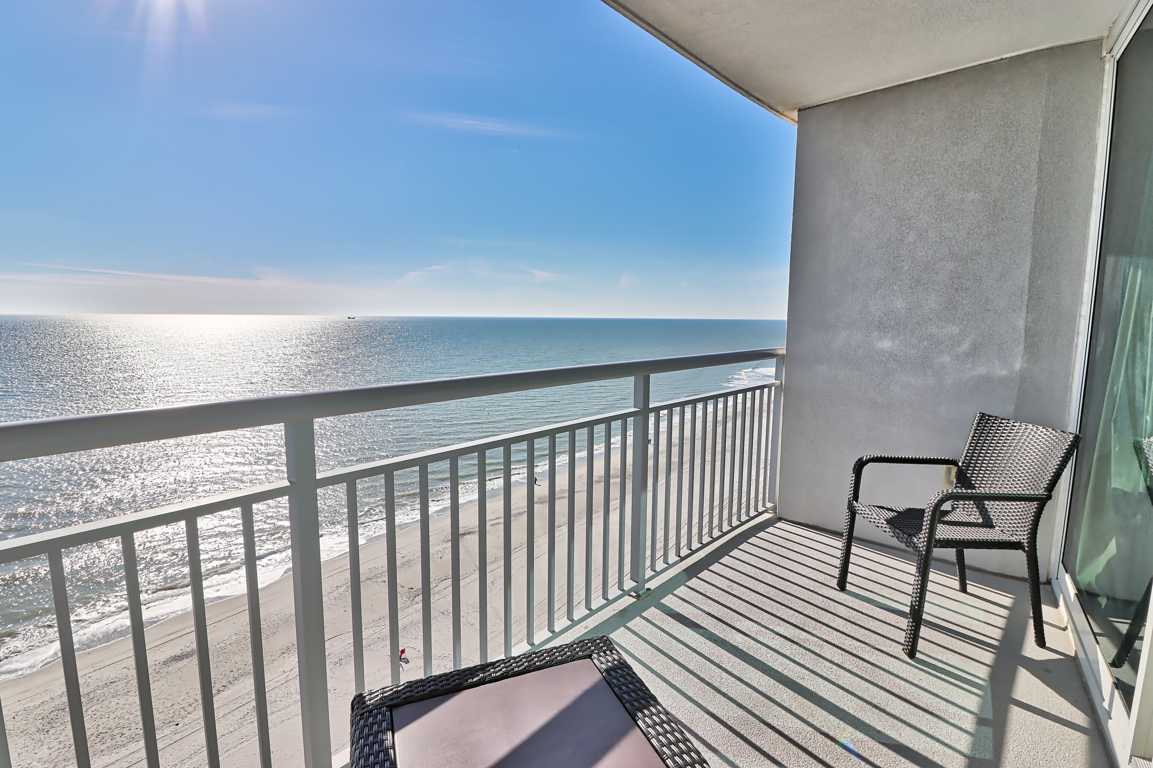A balcony with a view of the ocean, a chair, and a small table.