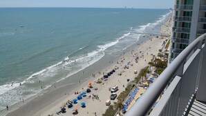 Une plage avec des parasols et des gens, un immeuble avec des balcons, et l’océan.