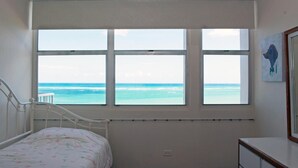 Une chambre avec une grande fenêtre donnant sur la mer, un lit avec une literie à motifs floraux et une petite table de chevet.